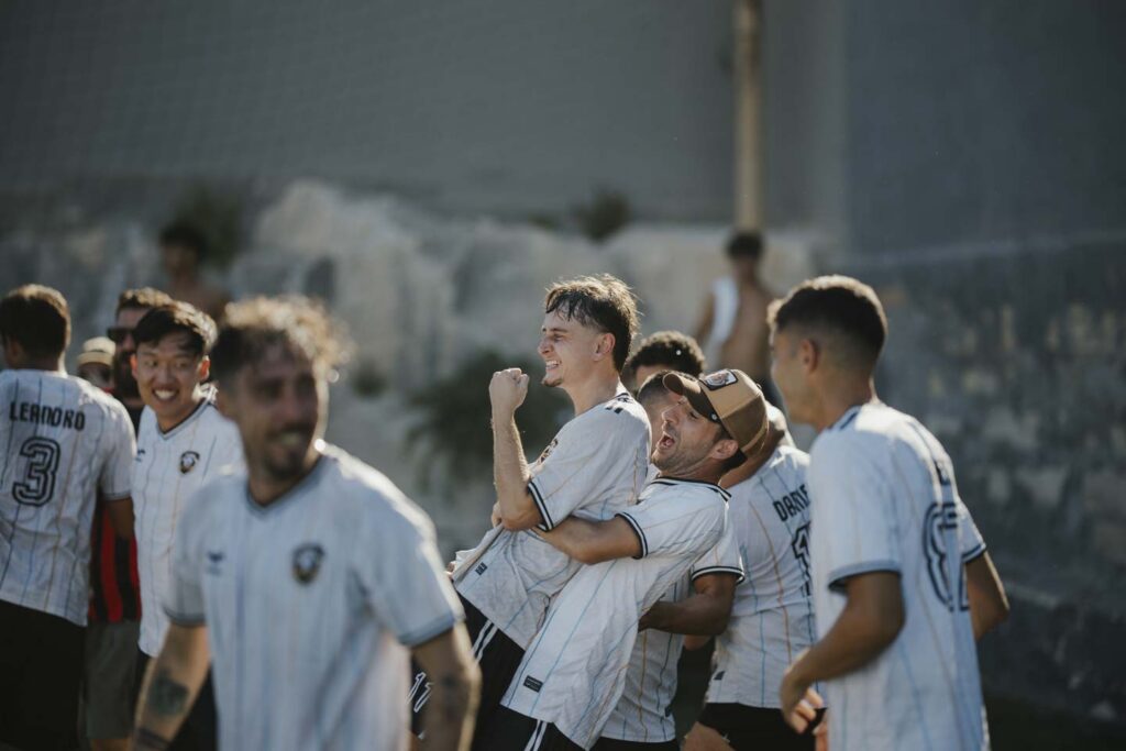 Neo Group players in celebrate joyfully on the field, with one player lifting his teammate in the air.